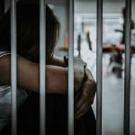 Person sitting behind metal bars looking down