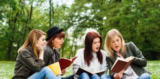 Four women reading books on a grassy field.