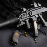 Black assault rifle with silencer and magazine on dark background.