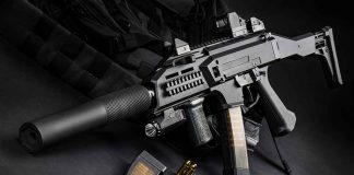 Black assault rifle with silencer and magazine on dark background.