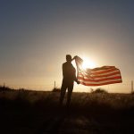 Person holding flag in sunset field silhouette sky