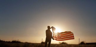 Person holding flag in sunset field silhouette sky