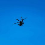 Silhouette of a helicopter against clear blue sky.