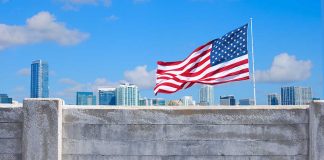 Man standing by tall concrete wall with American flag