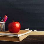 Apple on books with pencils beside a chalkboard.