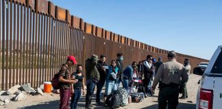 Group of people at border wall with patrol agents.
