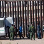 Border patrol officers detaining group near metal fence