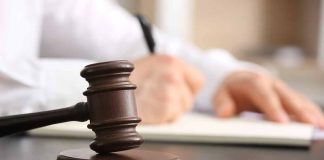 Judge's gavel on desk with person writing.