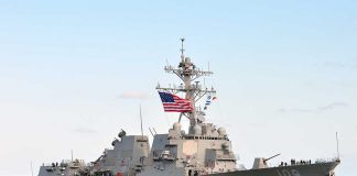Military ship sails with American flag.