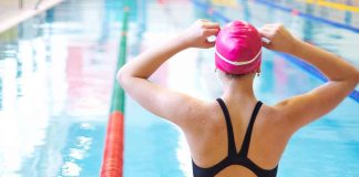 Swimmer adjusting cap near an indoor pool.
