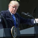 Man gesturing at two podiums outdoors.