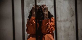 Person in orange jumpsuit sitting in a cell