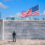 Man standing by tall concrete wall with American flag
