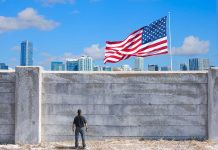 Man standing by tall concrete wall with American flag