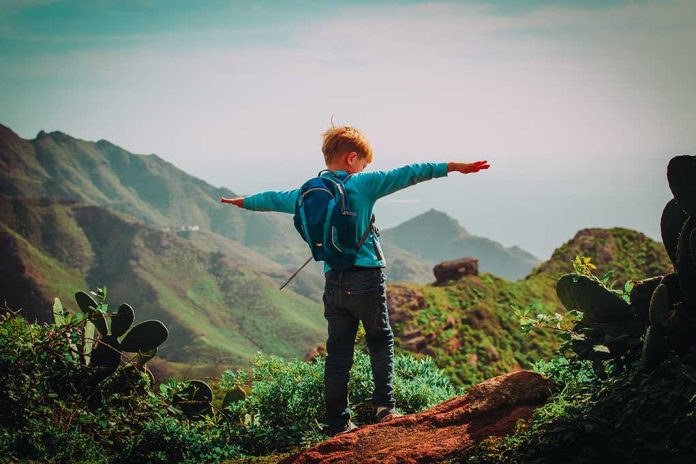 1020047392 featured image Child with backpack stands on mountain, arms outstretched.
