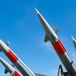 Four missiles pointing upwards under blue sky.