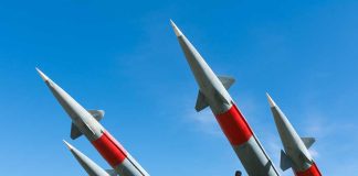 Four missiles pointing upwards under blue sky.