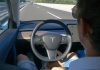 Person in Tesla car on autopilot, hands-free driving.