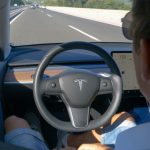 Person in Tesla car on autopilot, hands-free driving.