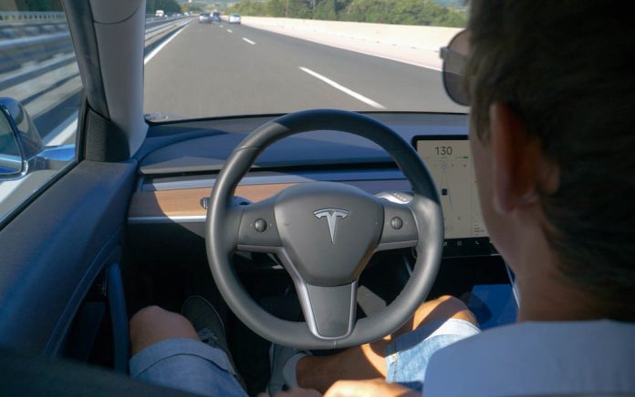 Person in Tesla car on autopilot, hands-free driving.