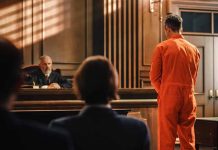 Man in orange jumpsuit stands in courtroom facing judge