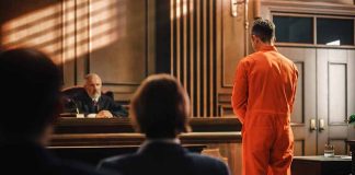 Man in orange jumpsuit stands in courtroom facing judge