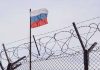 Barbed wire fence with a Russian flag above