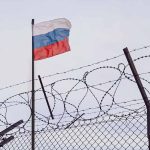 Barbed wire fence with a Russian flag above