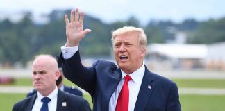 Man in suit waving while another man stands nearby