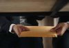 Two people exchanging envelope under table.