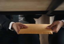 Two people exchanging envelope under table.