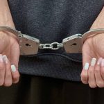 Hands with manicured nails in handcuffs.