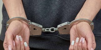 Hands with manicured nails in handcuffs.