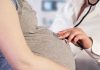 Doctor uses stethoscope on pregnant woman's belly.