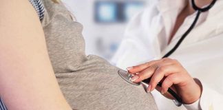 Doctor uses stethoscope on pregnant woman's belly.