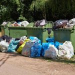 Overflowing garbage bins with bags on the ground.