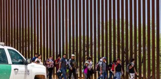 People walking beside tall fence and border patrol vehicle