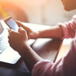 Person using smartphone while seated at a laptop