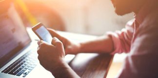Person using smartphone while seated at a laptop