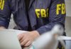 Person wearing FBI jacket using a laptop