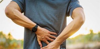 Person holding lower back in discomfort outdoors