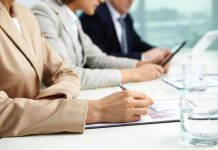 Close-up of hands in business attire during a meeting, writing notes and reviewing documents