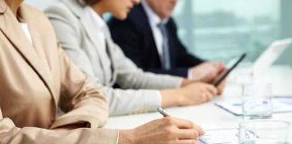 Close-up of hands in business attire during a meeting, writing notes and reviewing documents