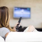 A woman sitting on a sofa holding a remote control and watching television
