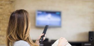 A woman sitting on a sofa holding a remote control and watching television
