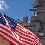American flags in front of a naval ship under a blue sky