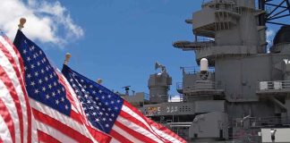 American flags in front of a naval ship under a blue sky