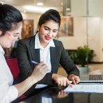 Two women discussing papers at a laptop