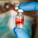 Gloved hand holding vial with red liquid and flag