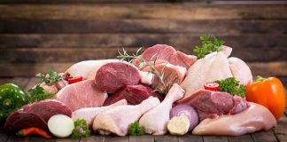 Assorted raw meat with vegetables on wooden table.